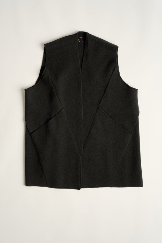 This image features the "Mundat Jacket," a stylish, sleeveless piece that boasts an architectural design with diagonal panels creating geometric pockets. The jacket is knitted in a structured jacquard, highlighted by its overlapping shoulder seams which add a distinctive touch to its silhouette.