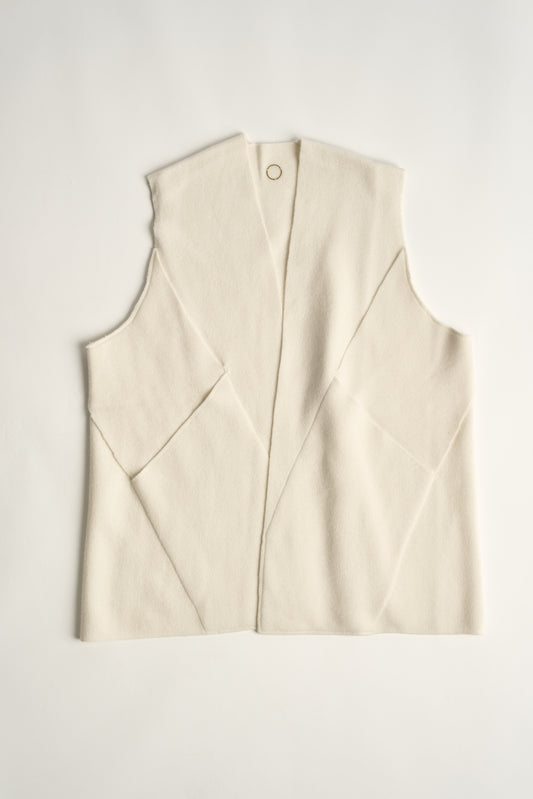 This image features the "Mundat Jacket," a stylish, sleeveless piece that boasts an architectural design with diagonal panels creating geometric pockets. The jacket is knitted in a structured jacquard, highlighted by its overlapping shoulder seams which add a distinctive touch to its silhouette.