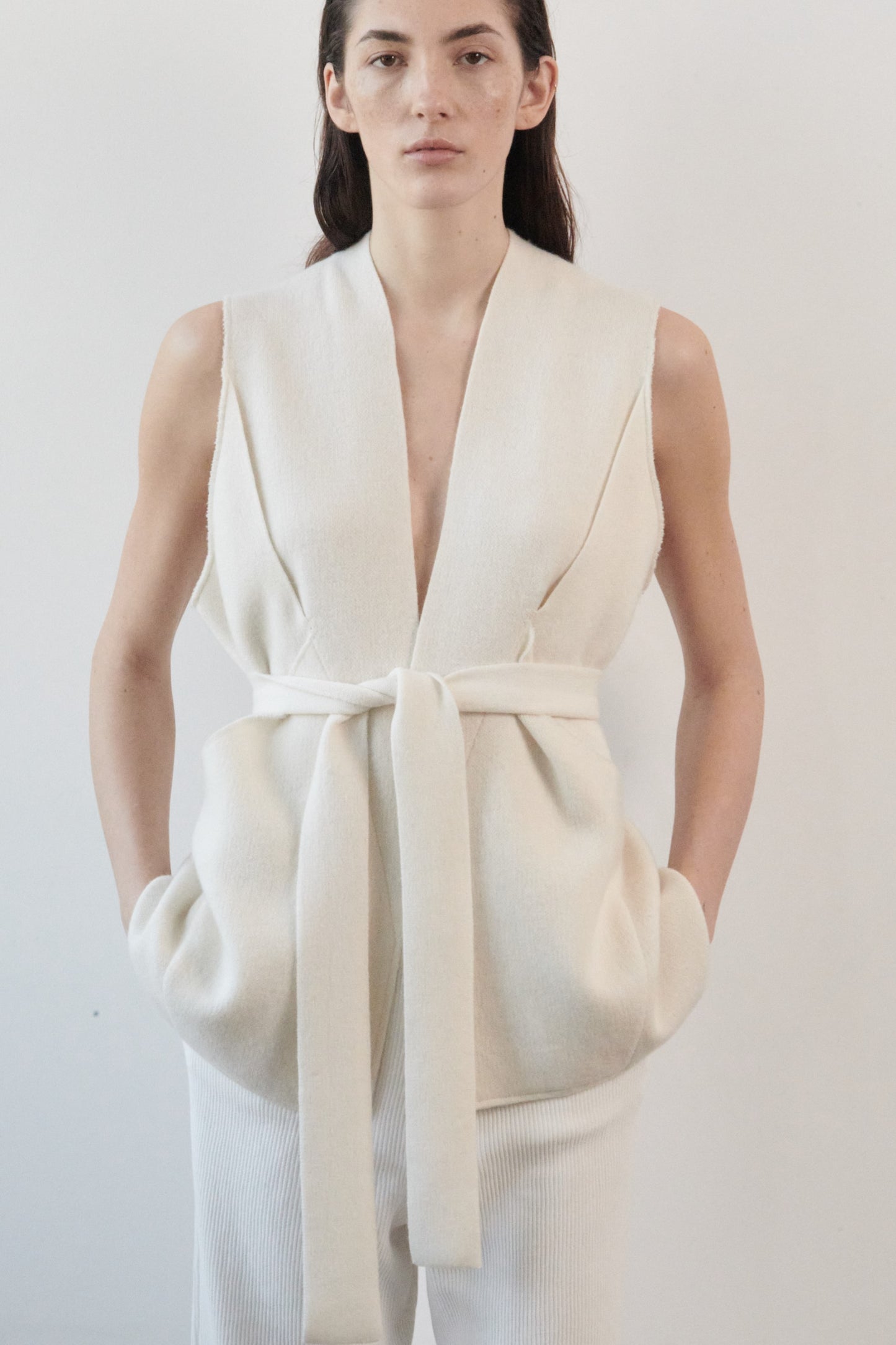 This image features the "Mundat Jacket," a stylish, sleeveless piece that boasts an architectural design with diagonal panels creating geometric pockets. The jacket is knitted in a structured jacquard, highlighted by its overlapping shoulder seams which add a distinctive touch to its silhouette.