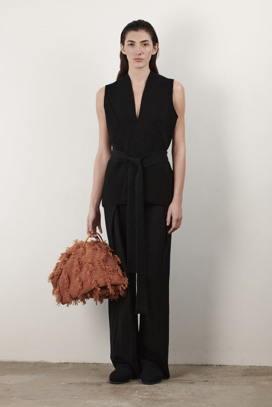 This image features the "Mundat Jacket," a stylish, sleeveless piece that boasts an architectural design with diagonal panels creating geometric pockets. The jacket is knitted in a structured jacquard, highlighted by its overlapping shoulder seams which add a distinctive touch to its silhouette.