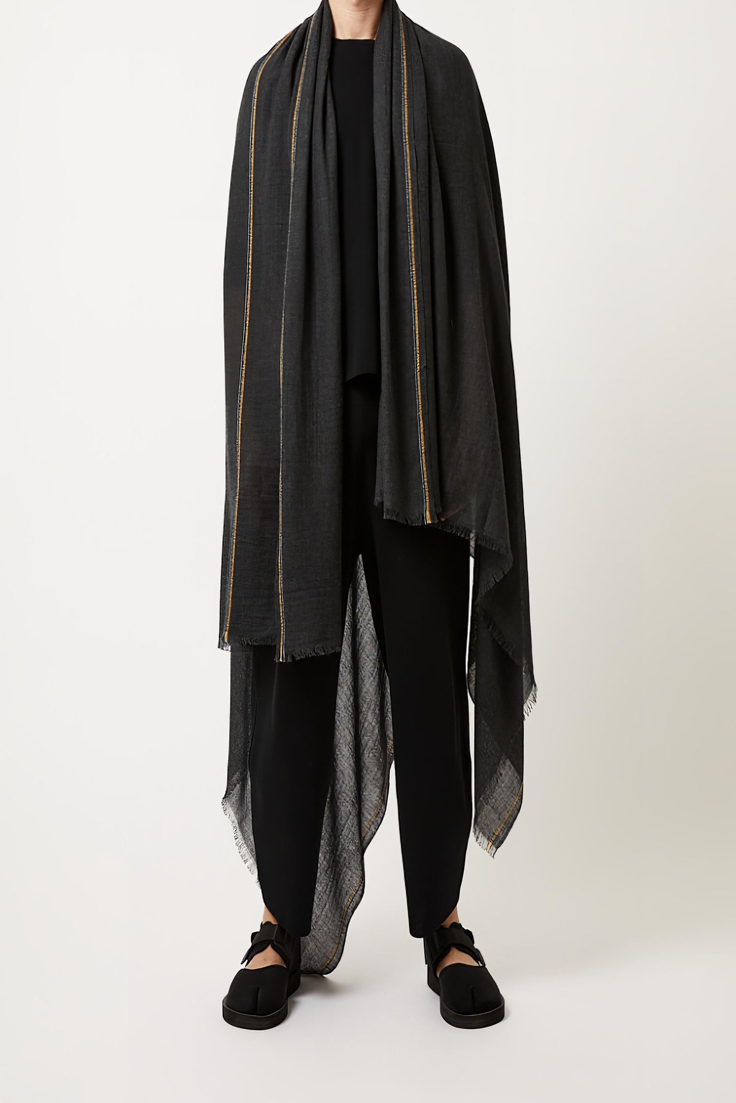 A charcoal cashmere travel throw with visible fringes, draped over the models shoulders