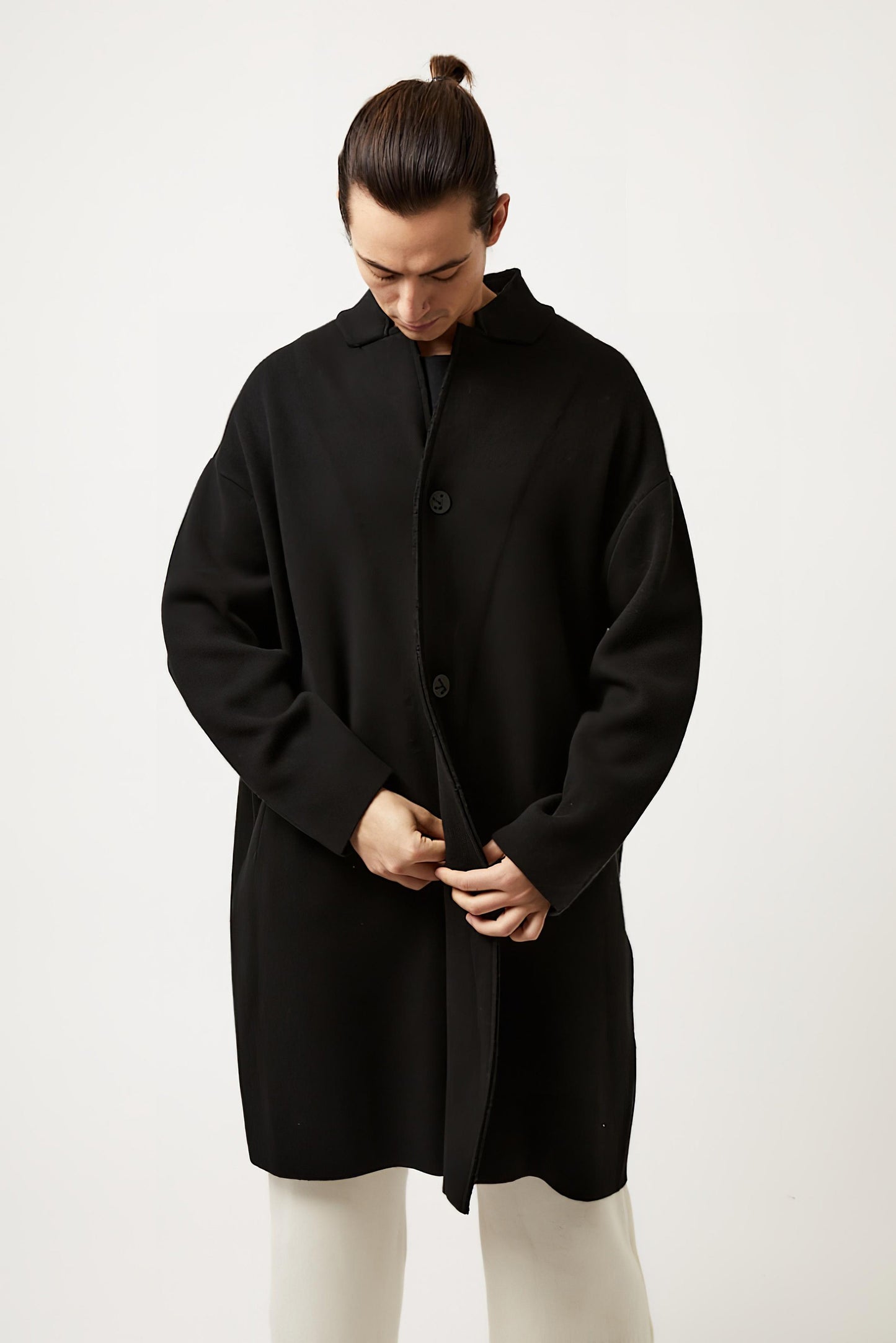 This image features a model wearing the Storm Coat by Oyuna, which showcases an elegant and practical design. The coat is black, knitted in a structured jacquard knit, and exhibits an oversized fit with a stand-up collar, enhancing its stylish appearance.