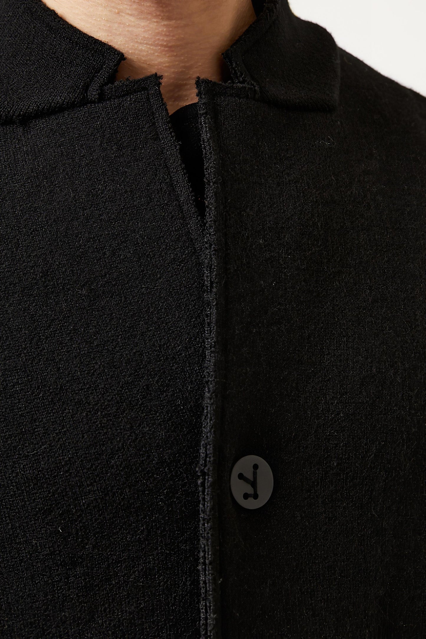 This image features a model wearing the Storm Coat by Oyuna, which showcases an elegant and practical design. The coat is black, knitted in a structured jacquard knit, and exhibits an oversized fit with a stand-up collar, enhancing its stylish appearance.