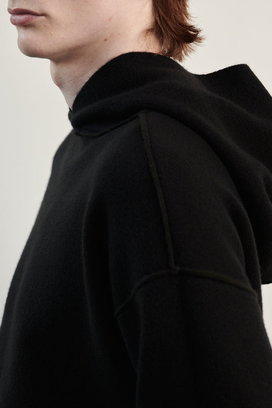A close up image featuring a luxurious black cashmere hoodie, displayed against a neutral background to emphasize its design and color. The hoodie boasts a modern and minimalist look, with a soft and snug fit that promises comfort and style.