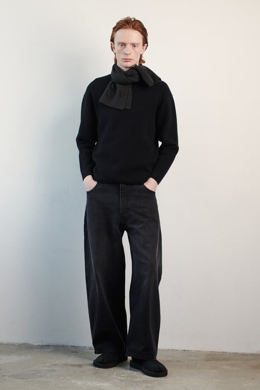 This image features the Axa Sweater, highlighted in a minimalistic style with a black color. The sweater showcases an oversized fit with distinct drop shoulders and sculpted, rounded sleeves.