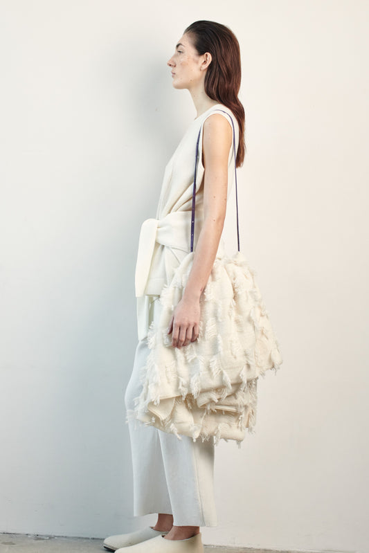 This image features the Duon Top, a stylish and comfortable cashmere knit vest in a subtle ivory color. The vest is designed with a boxy silhouette and fitted shoulders, creating a relaxed yet fitted look.