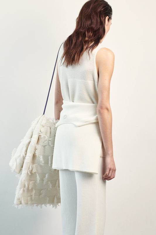 This image features the Duon Top, a stylish and comfortable cashmere knit vest in a subtle ivory color. The vest is designed with a boxy silhouette and fitted shoulders, creating a relaxed yet fitted look.