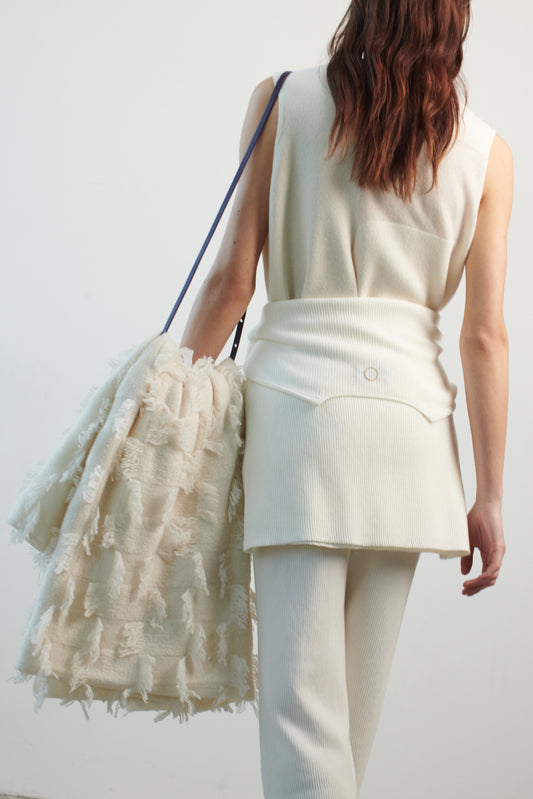 This image features the Duon Top, a stylish and comfortable cashmere knit vest in a subtle ivory color. The vest is designed with a boxy silhouette and fitted shoulders, creating a relaxed yet fitted look.