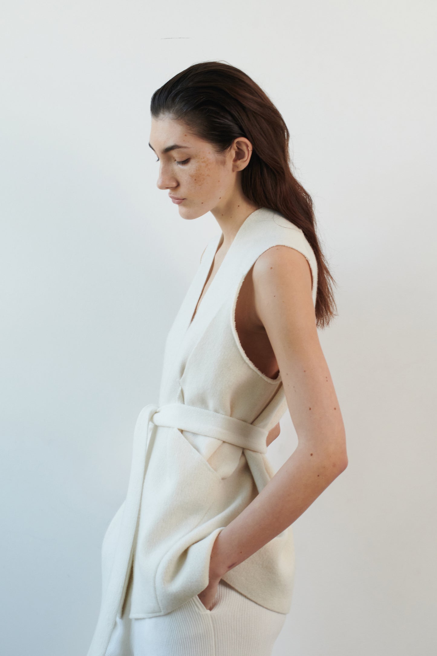 This image features the "Mundat Jacket," a stylish, sleeveless piece that boasts an architectural design with diagonal panels creating geometric pockets. The jacket is knitted in a structured jacquard, highlighted by its overlapping shoulder seams which add a distinctive touch to its silhouette.