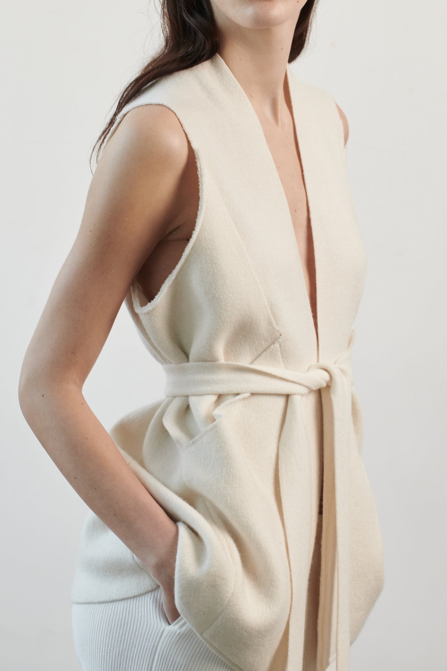 This image features the "Mundat Jacket," a stylish, sleeveless piece that boasts an architectural design with diagonal panels creating geometric pockets. The jacket is knitted in a structured jacquard, highlighted by its overlapping shoulder seams which add a distinctive touch to its silhouette.