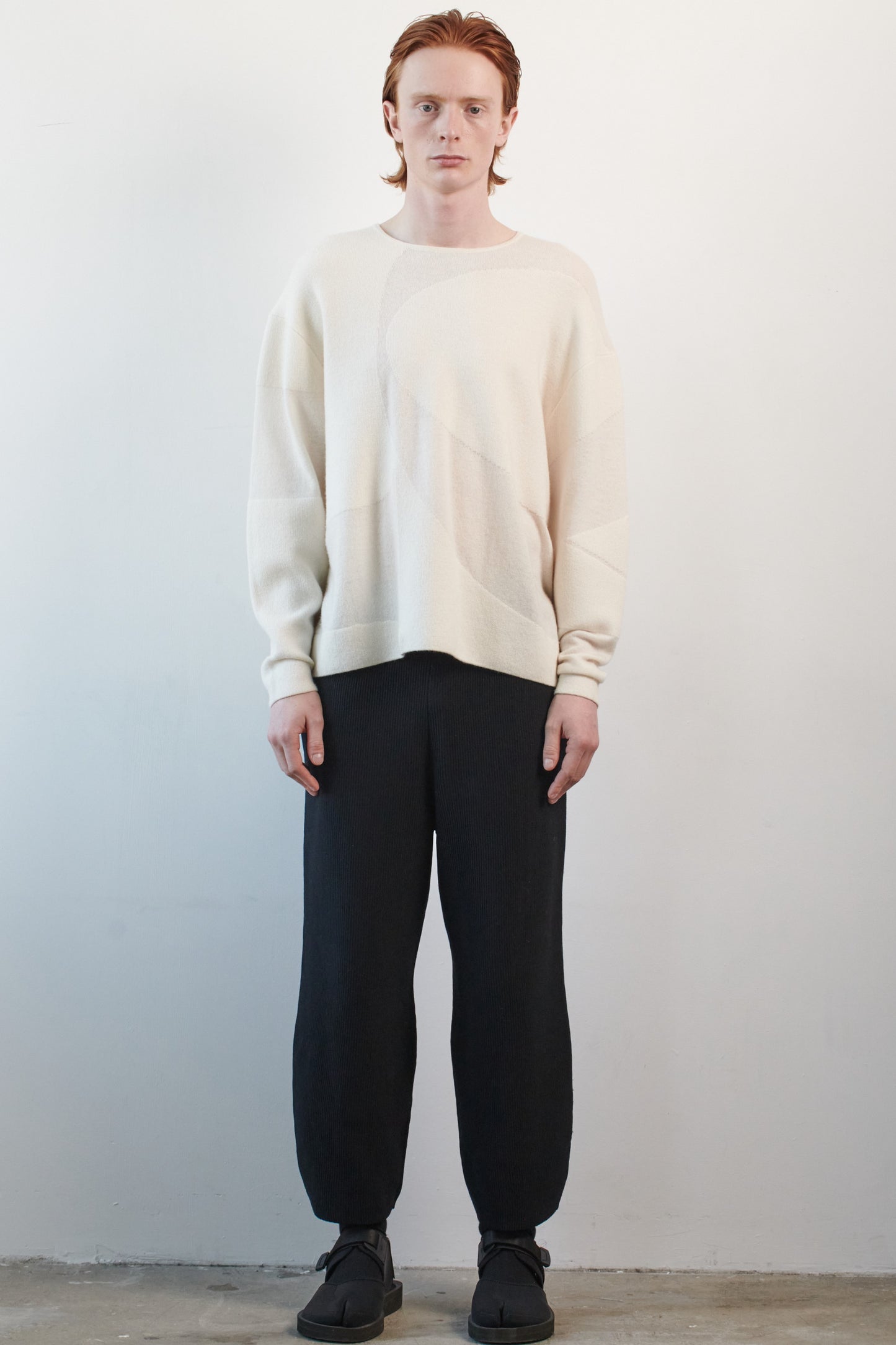 This image features the Arouc Sweater, a stylish and cozy garment that embodies a relaxed, everyday aesthetic. The sweater displays a boxy silhouette, crafted in a knitted jacquard print that forms an abstract, organic pattern in shades of ivory and feather.