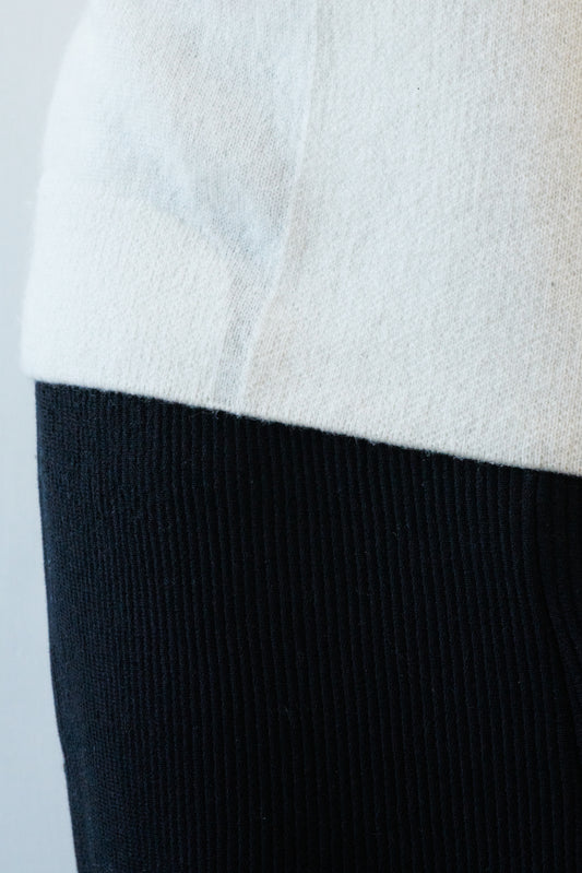 This image features the Arouc Sweater, a stylish and cozy garment that embodies a relaxed, everyday aesthetic. The sweater displays a boxy silhouette, crafted in a knitted jacquard print that forms an abstract, organic pattern in shades of ivory and feather.