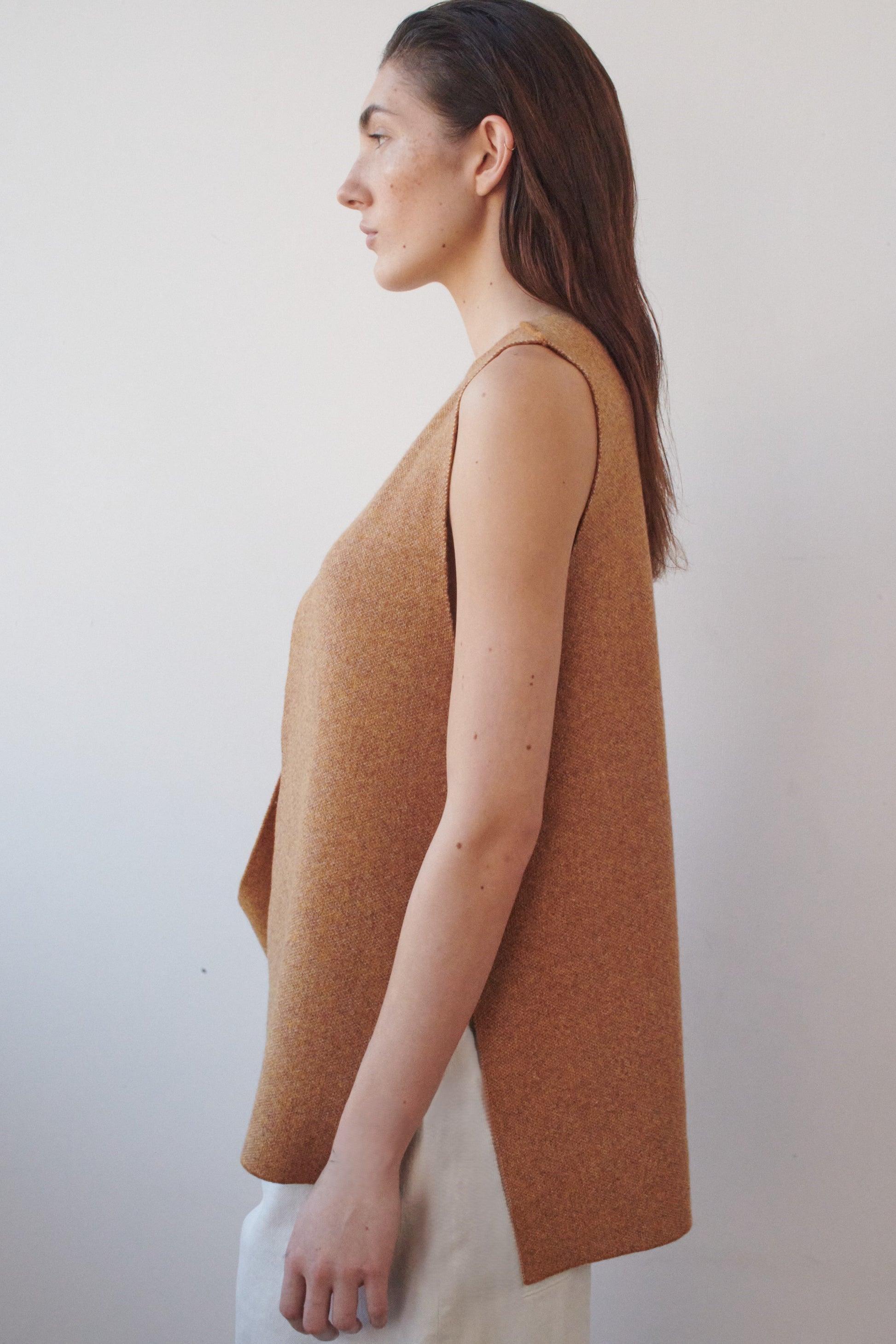This image features the Ayal Jacket, a stylish sleeveless cashmere jacket displayed on a female model. The jacket is characterized by its asymmetric design, with a distinctive slit on the front left panel and button details on the front hem, adding a touch of uniqueness to its appearance.