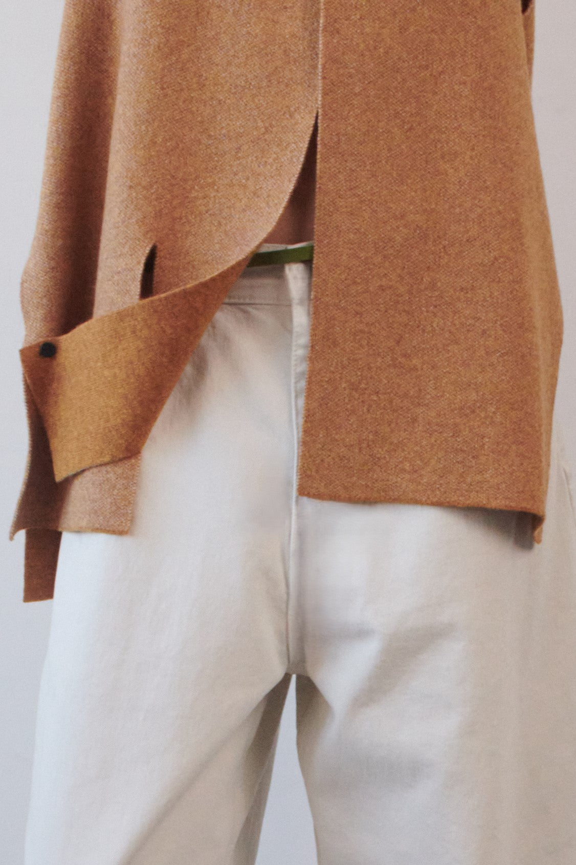 This image features the Ayal Jacket, a stylish sleeveless cashmere jacket displayed on a female model. The jacket is characterized by its asymmetric design, with a distinctive slit on the front left panel and button details on the front hem, adding a touch of uniqueness to its appearance.