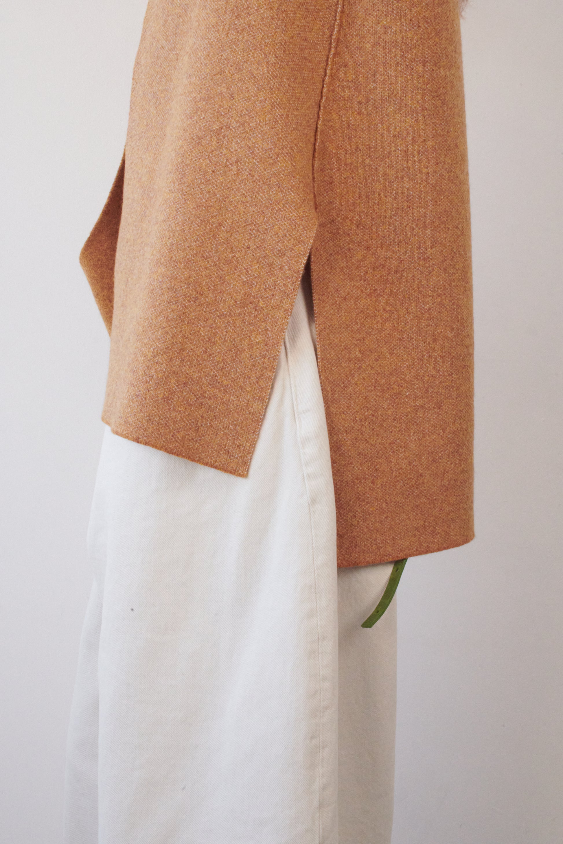 This image features the Ayal Jacket, a stylish sleeveless cashmere jacket displayed on a female model. The jacket is characterized by its asymmetric design, with a distinctive slit on the front left panel and button details on the front hem, adding a touch of uniqueness to its appearance.