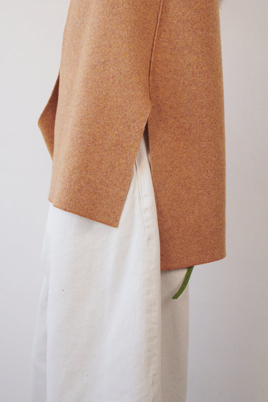This image features the Ayal Jacket, a stylish sleeveless cashmere jacket displayed on a female model. The jacket is characterized by its asymmetric design, with a distinctive slit on the front left panel and button details on the front hem, adding a touch of uniqueness to its appearance.