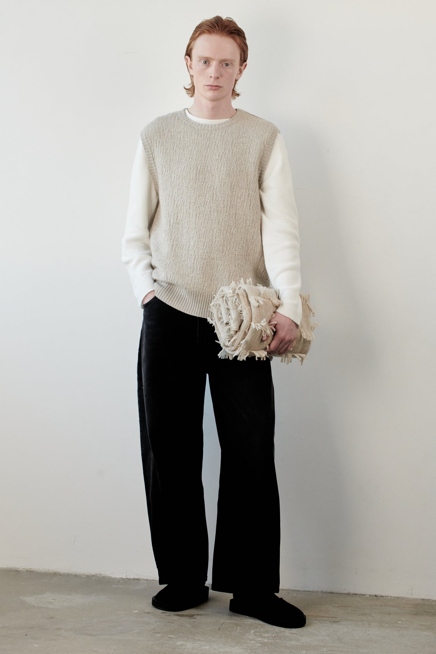 This image features the Terra Top, a stylish knitted texture vest crafted from 100% cashmere, providing an unmatched softness and warmth. The model is seen wearing the vest in a layering style over a cream-colored sweater, paired with dark trousers, showcasing the vest's sophisticated and subtle textured design.