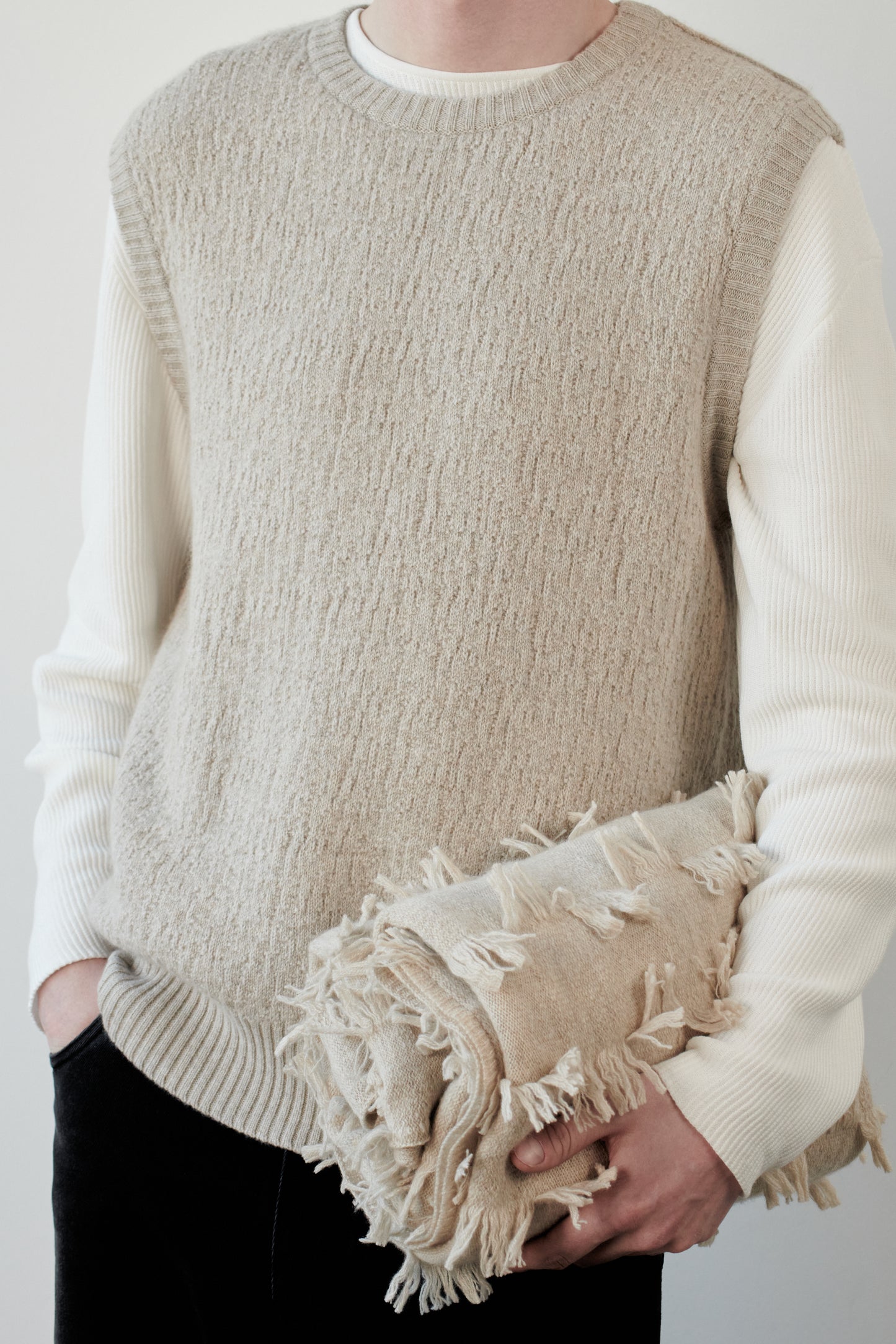 This image features the Terra Top, a stylish knitted texture vest crafted from 100% cashmere, providing an unmatched softness and warmth. The model is seen wearing the vest in a layering style over a cream-colored sweater, paired with dark trousers, showcasing the vest's sophisticated and subtle textured design.