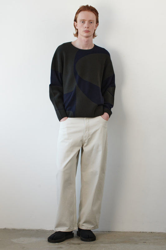 This image features the Arouc Sweater, a stylish and cozy garment that embodies a relaxed, everyday aesthetic. The sweater displays a boxy silhouette, crafted in a knitted jacquard print that forms an abstract, organic pattern in shades of green and navy blue.