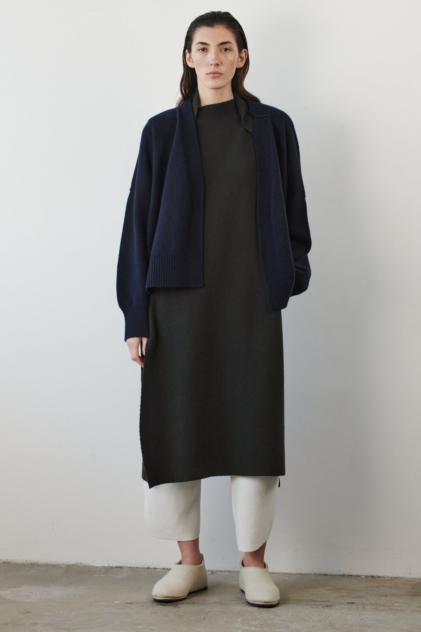 This image features the Aire Cardigan, a luxurious, chunky open cardigan made from pure cashmere. The cardigan is displayed on a model, showcasing its sleek ocean color and stylish design elements.