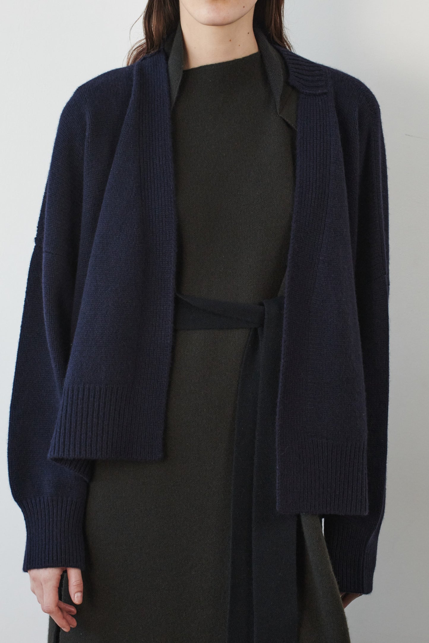 This image features the Aire Cardigan, a luxurious, chunky open cardigan made from pure cashmere. The cardigan is displayed on a model, showcasing its sleek ocean color and stylish design elements.
