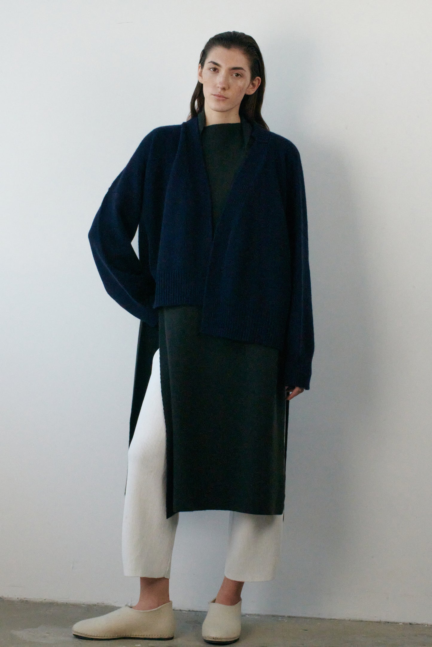 This image features the Aire Cardigan, a luxurious, chunky open cardigan made from pure cashmere. The cardigan is displayed on a model, showcasing its sleek ocean color and stylish design elements.