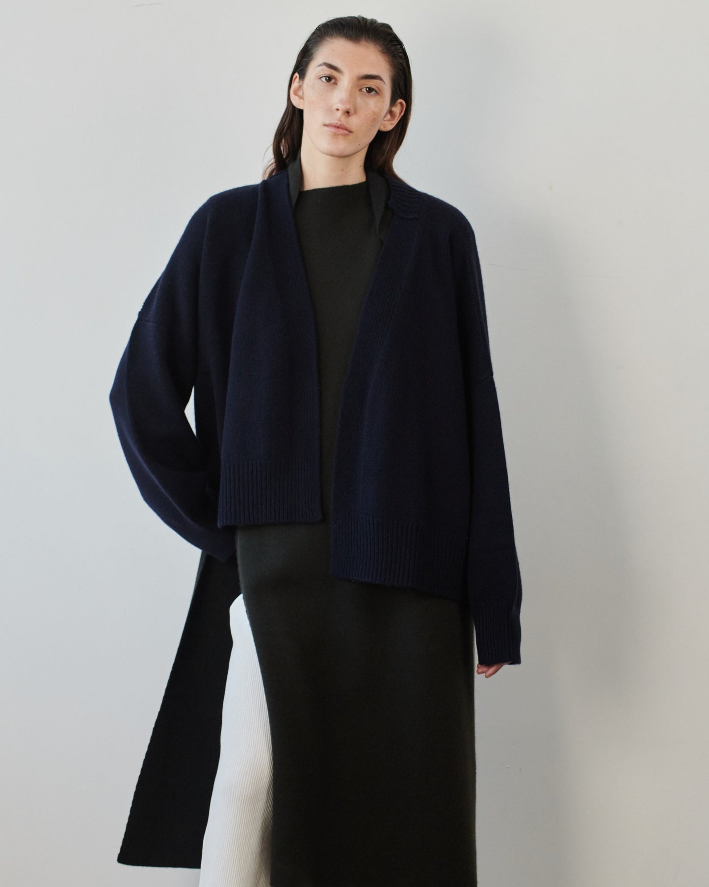 This image features the Aire Cardigan, a luxurious, chunky open cardigan made from pure cashmere. The cardigan is displayed on a model, showcasing its sleek ocean color and stylish design elements.