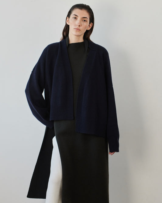 This image features the Aire Cardigan, a luxurious, chunky open cardigan made from pure cashmere. The cardigan is displayed on a model, showcasing its sleek ocean color and stylish design elements.