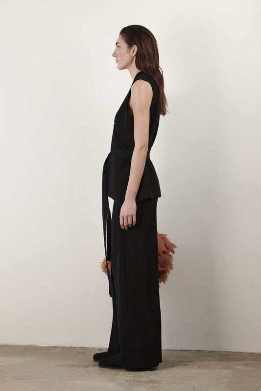 This image features the "Mundat Jacket," a stylish, sleeveless piece that boasts an architectural design with diagonal panels creating geometric pockets. The jacket is knitted in a structured jacquard, highlighted by its overlapping shoulder seams which add a distinctive touch to its silhouette.