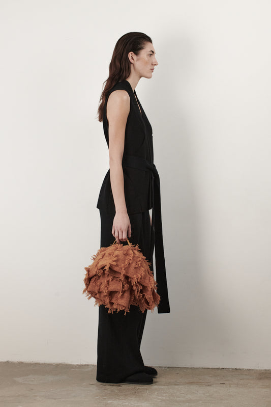 This image features the "Mundat Jacket," a stylish, sleeveless piece that boasts an architectural design with diagonal panels creating geometric pockets. The jacket is knitted in a structured jacquard, highlighted by its overlapping shoulder seams which add a distinctive touch to its silhouette.