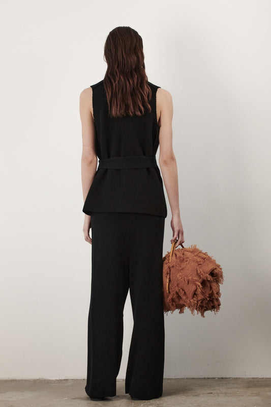 This image features the "Mundat Jacket," a stylish, sleeveless piece that boasts an architectural design with diagonal panels creating geometric pockets. The jacket is knitted in a structured jacquard, highlighted by its overlapping shoulder seams which add a distinctive touch to its silhouette.