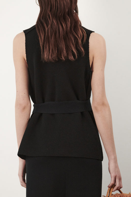 This image features the "Mundat Jacket," a stylish, sleeveless piece that boasts an architectural design with diagonal panels creating geometric pockets. The jacket is knitted in a structured jacquard, highlighted by its overlapping shoulder seams which add a distinctive touch to its silhouette.