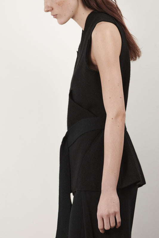 This image features the "Mundat Jacket," a stylish, sleeveless piece that boasts an architectural design with diagonal panels creating geometric pockets. The jacket is knitted in a structured jacquard, highlighted by its overlapping shoulder seams which add a distinctive touch to its silhouette.