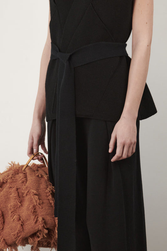 This image features the "Mundat Jacket," a stylish, sleeveless piece that boasts an architectural design with diagonal panels creating geometric pockets. The jacket is knitted in a structured jacquard, highlighted by its overlapping shoulder seams which add a distinctive touch to its silhouette.