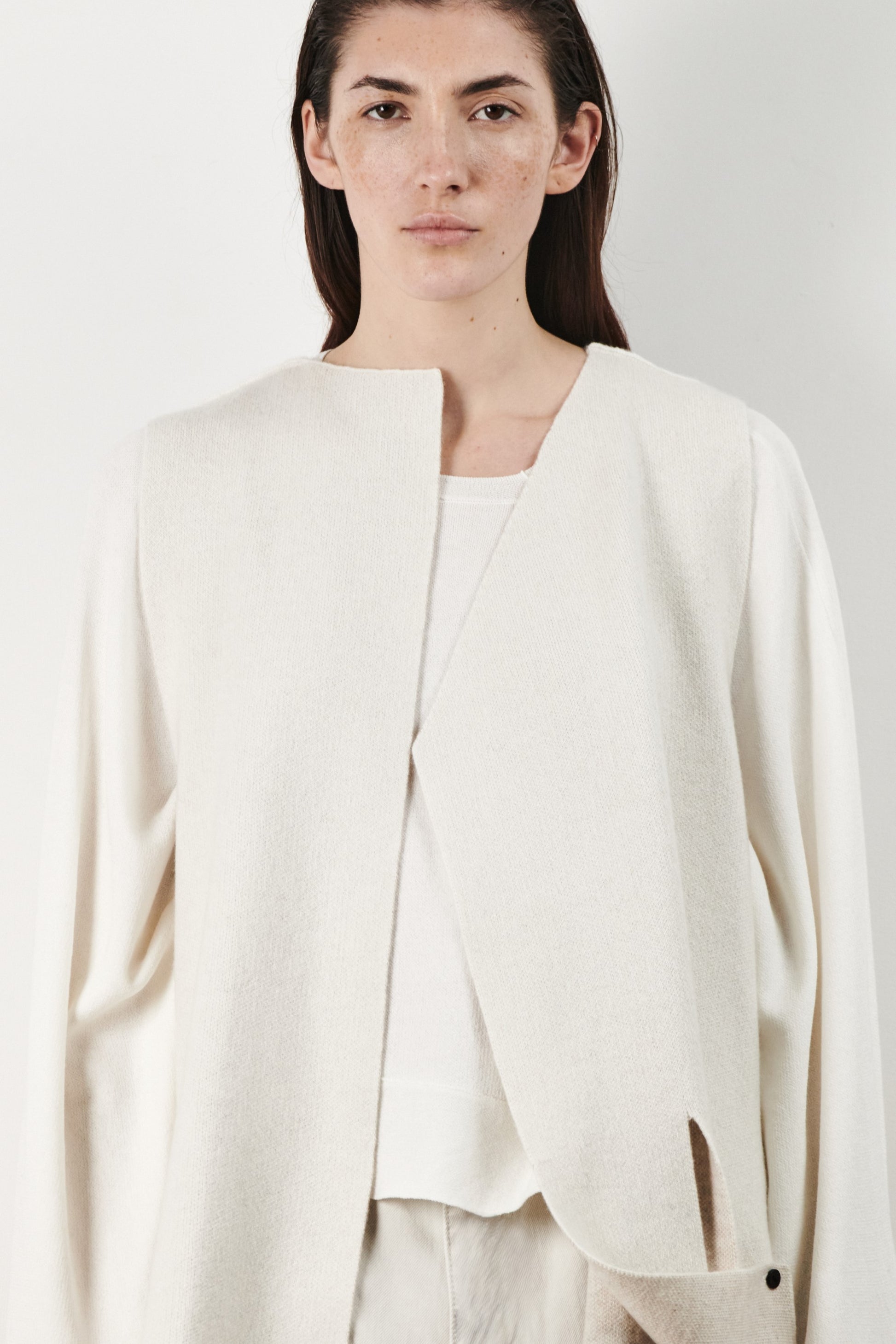 This image features the Ayal Jacket, a stylish sleeveless cashmere jacket displayed on a female model. The jacket is characterized by its asymmetric design, with a distinctive slit on the front left panel and button details on the front hem, adding a touch of uniqueness to its appearance.