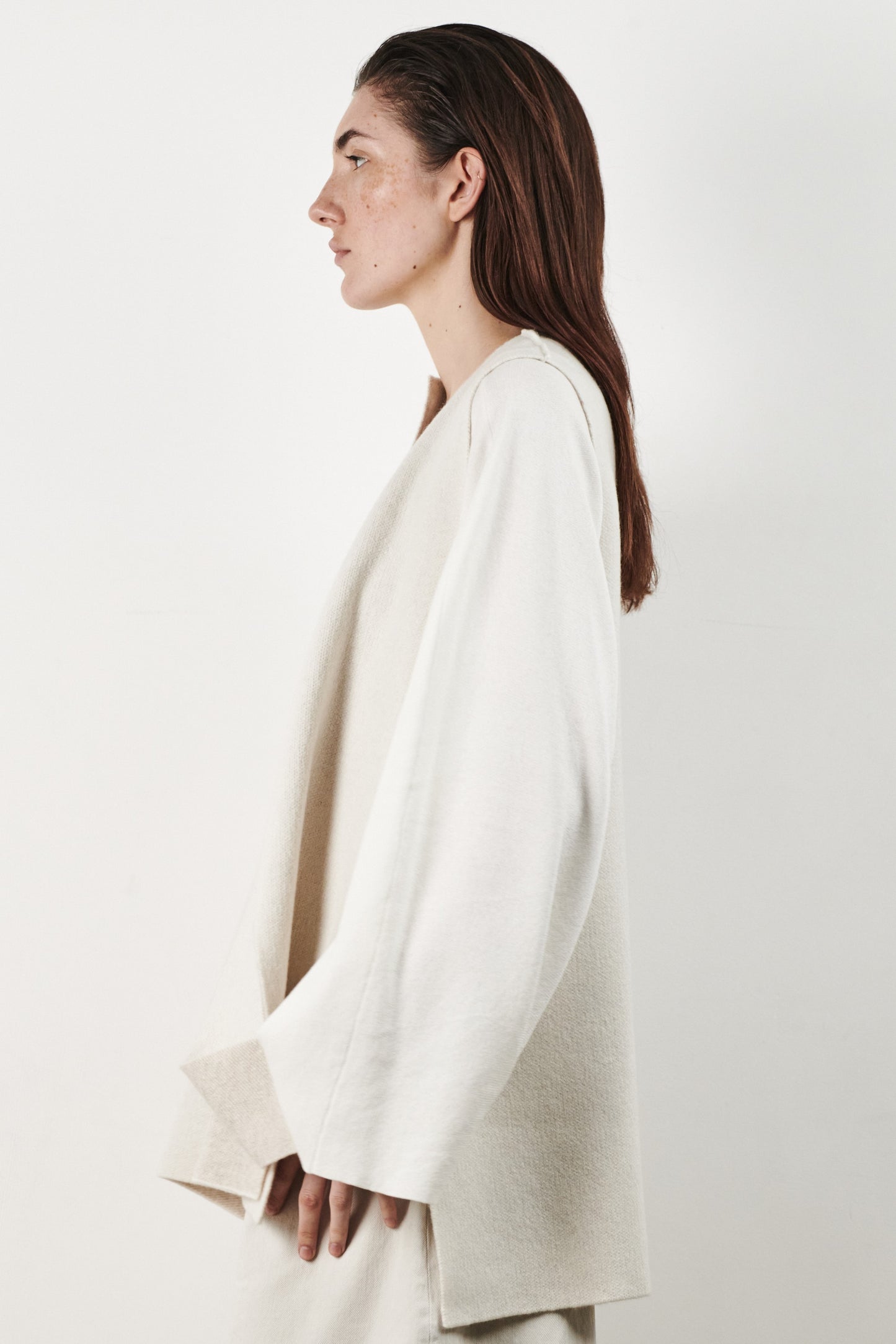This image features the Ayal Jacket, a stylish sleeveless cashmere jacket displayed on a female model. The jacket is characterized by its asymmetric design, with a distinctive slit on the front left panel and button details on the front hem, adding a touch of uniqueness to its appearance.