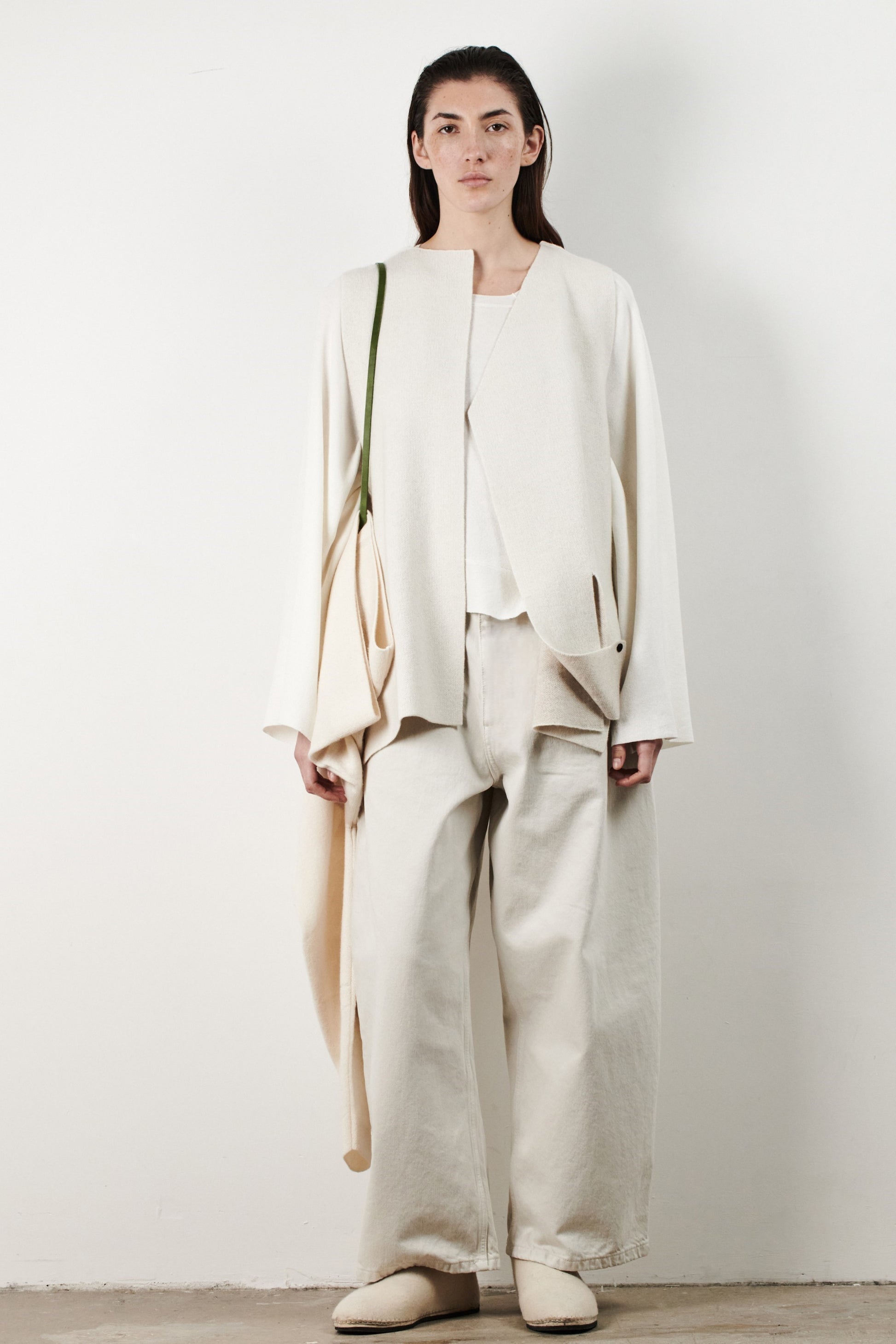 This image features the Ayal Jacket, a stylish sleeveless cashmere jacket displayed on a female model. The jacket is characterized by its asymmetric design, with a distinctive slit on the front left panel and button details on the front hem, adding a touch of uniqueness to its appearance.