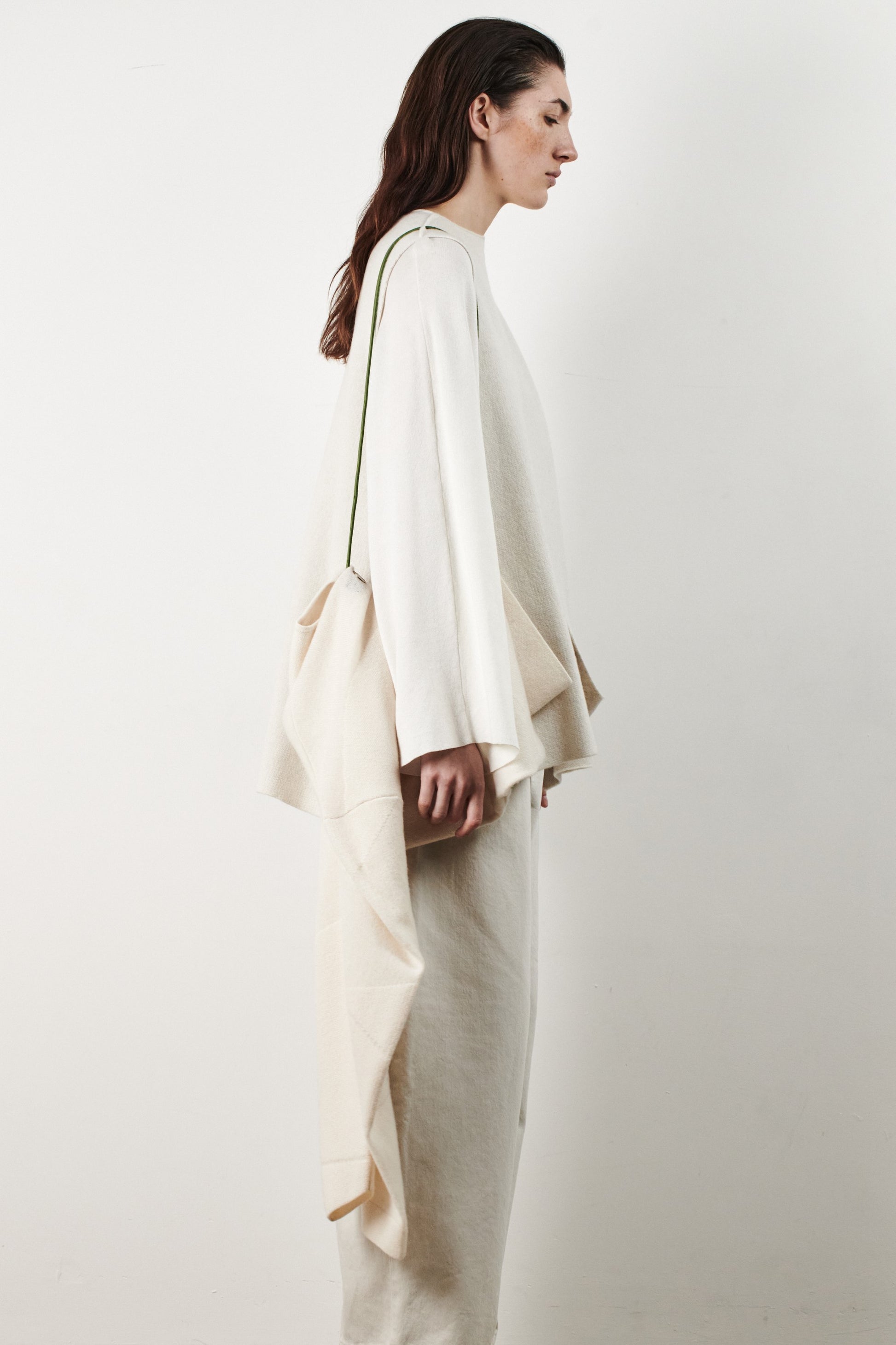 This image features the Ayal Jacket, a stylish sleeveless cashmere jacket displayed on a female model. The jacket is characterized by its asymmetric design, with a distinctive slit on the front left panel and button details on the front hem, adding a touch of uniqueness to its appearance.