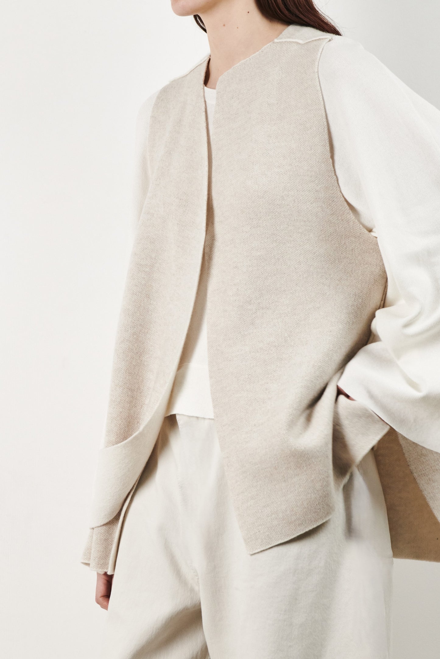 This image features the Ayal Jacket, a stylish sleeveless cashmere jacket displayed on a female model. The jacket is characterized by its asymmetric design, with a distinctive slit on the front left panel and button details on the front hem, adding a touch of uniqueness to its appearance.