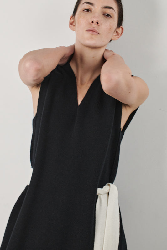 This image features the Mauni Dress, a stylish sleeveless V-neck dress crafted in a jacquard knit. The dress displays an elegant and modern silhouette, highlighted by its intricate texture and a sleek, contrasting belt that enhances the waistline.