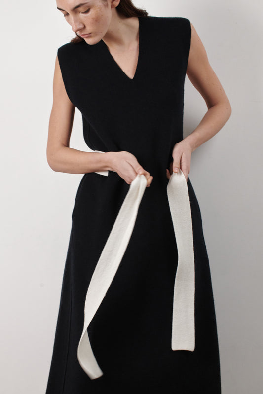 This image features the Mauni Dress, a stylish sleeveless V-neck dress crafted in a jacquard knit. The dress displays an elegant and modern silhouette, highlighted by its intricate texture and a sleek, contrasting belt that enhances the waistline.