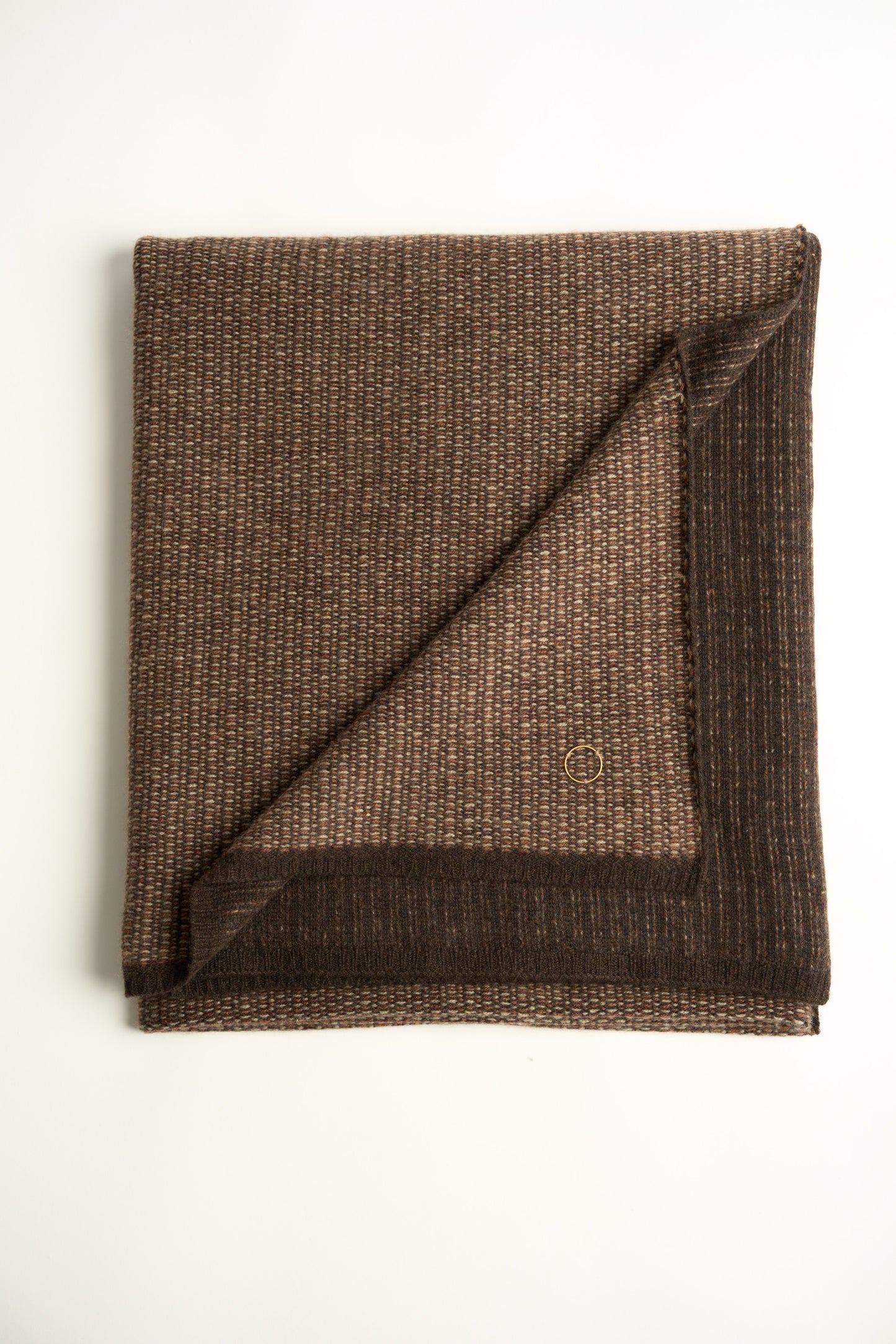 This image features the Quadro Throw, a knitted square knit throw that exudes warmth and texture. Its soft, cozy texture is highlighted by the gentle folds and the neutral, warm brown color that complements any room.