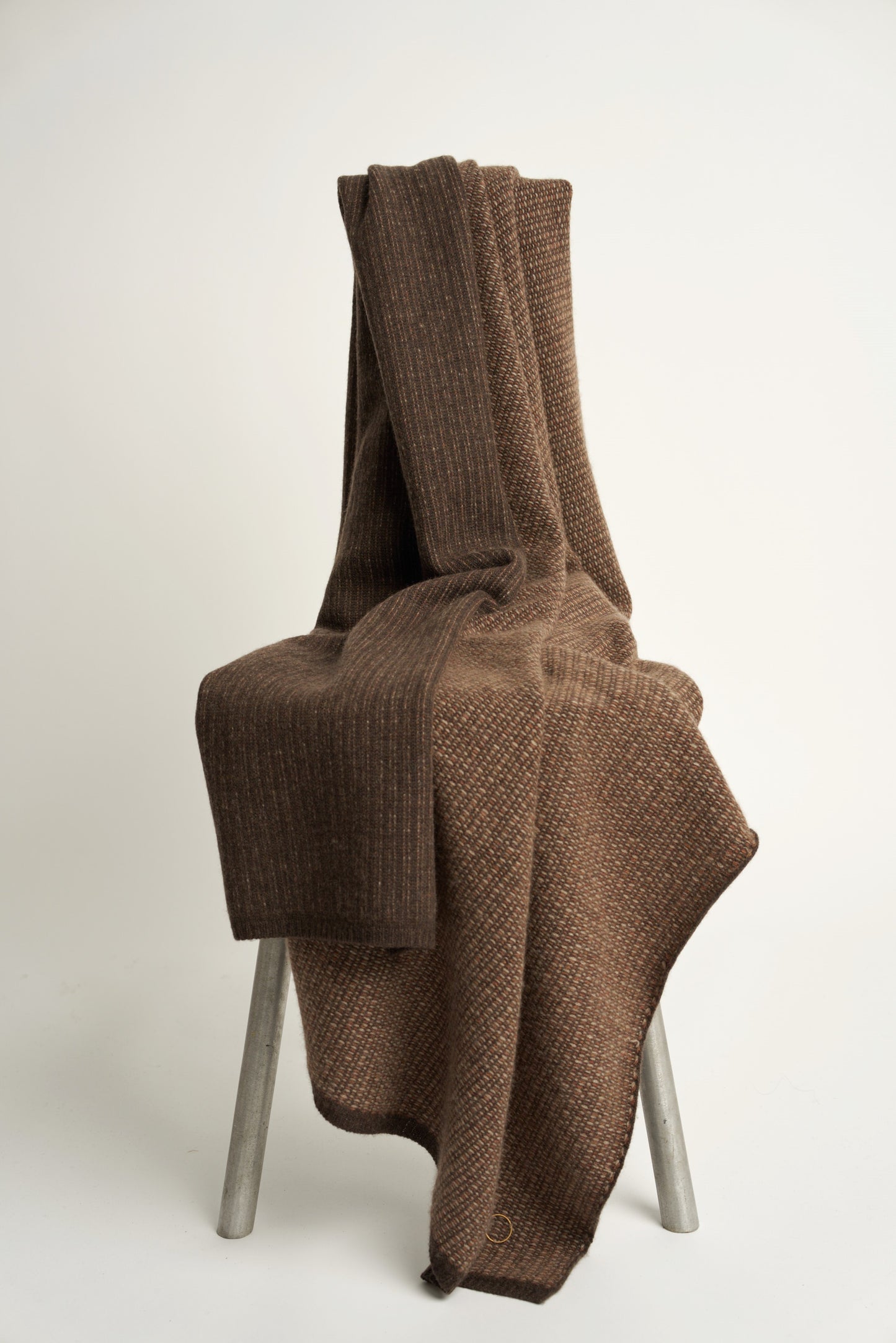 This image features the Quadro Throw, a knitted square knit throw that exudes warmth and texture. Its soft, cozy texture is highlighted by the gentle folds and the neutral, warm brown color that complements any room.