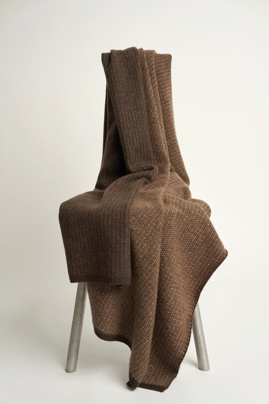 This image features the Quadro Throw, a knitted square knit throw that exudes warmth and texture. Its soft, cozy texture is highlighted by the gentle folds and the neutral, warm brown color that complements any room.