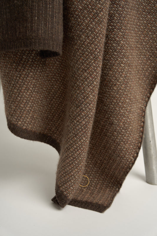 This image features the Quadro Throw, a knitted square knit throw that exudes warmth and texture. Its soft, cozy texture is highlighted by the gentle folds and the neutral, warm brown color that complements any room.