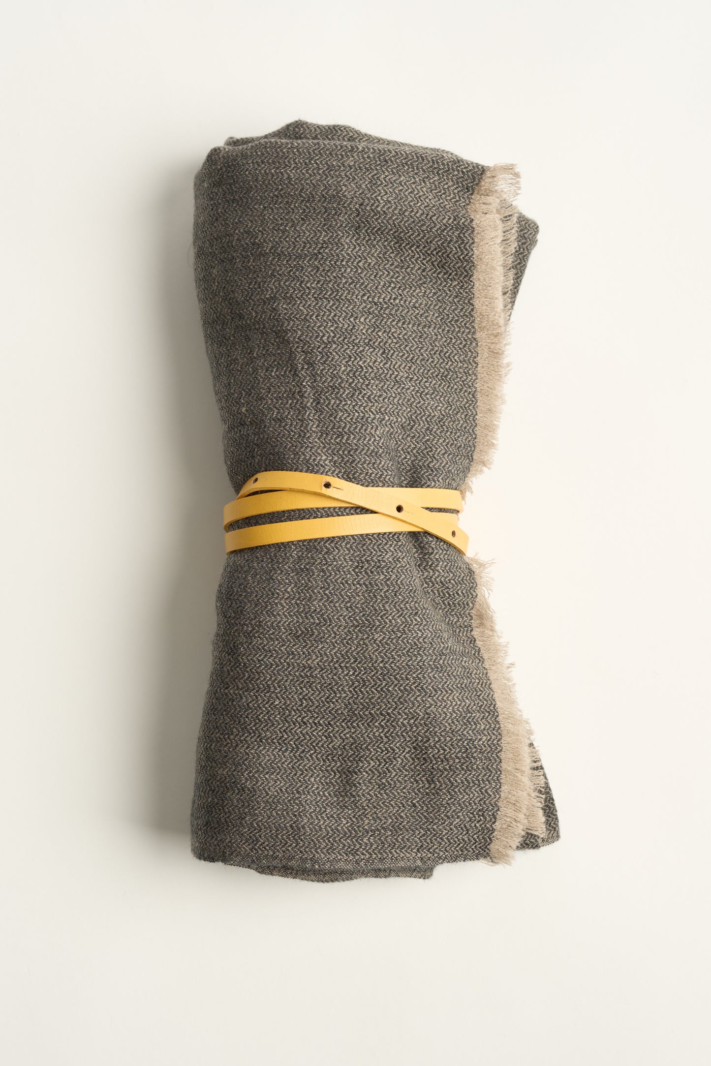 A charcoal and taupe saan throw, tied with a gold leather belt on a white background