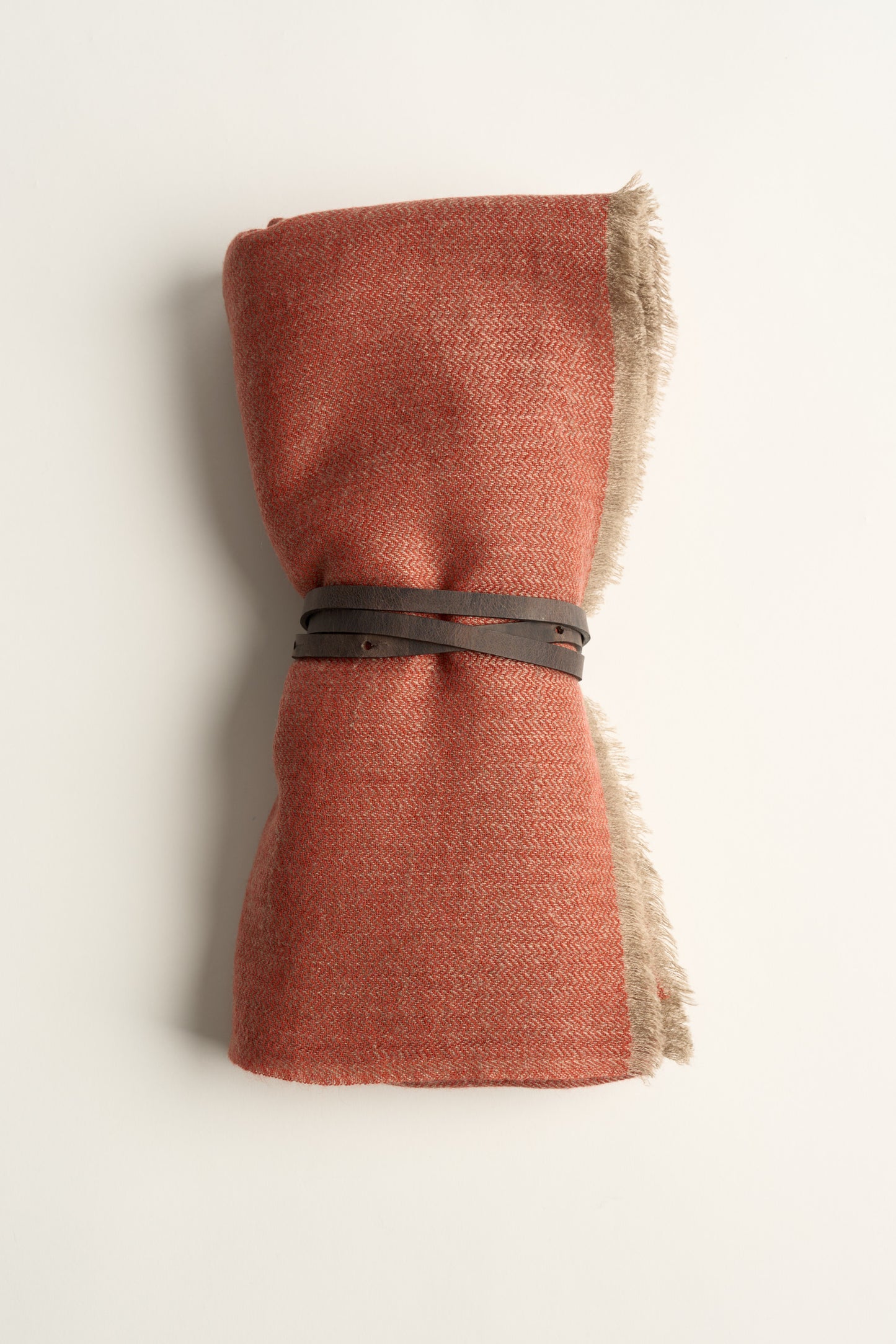 A coral and taupe saan throw, tied with a brown leather belt on a white background