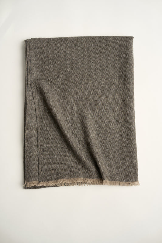 A folded charcoal Saan throw with a herringbone pattern, featuring soft fringing at the edges.