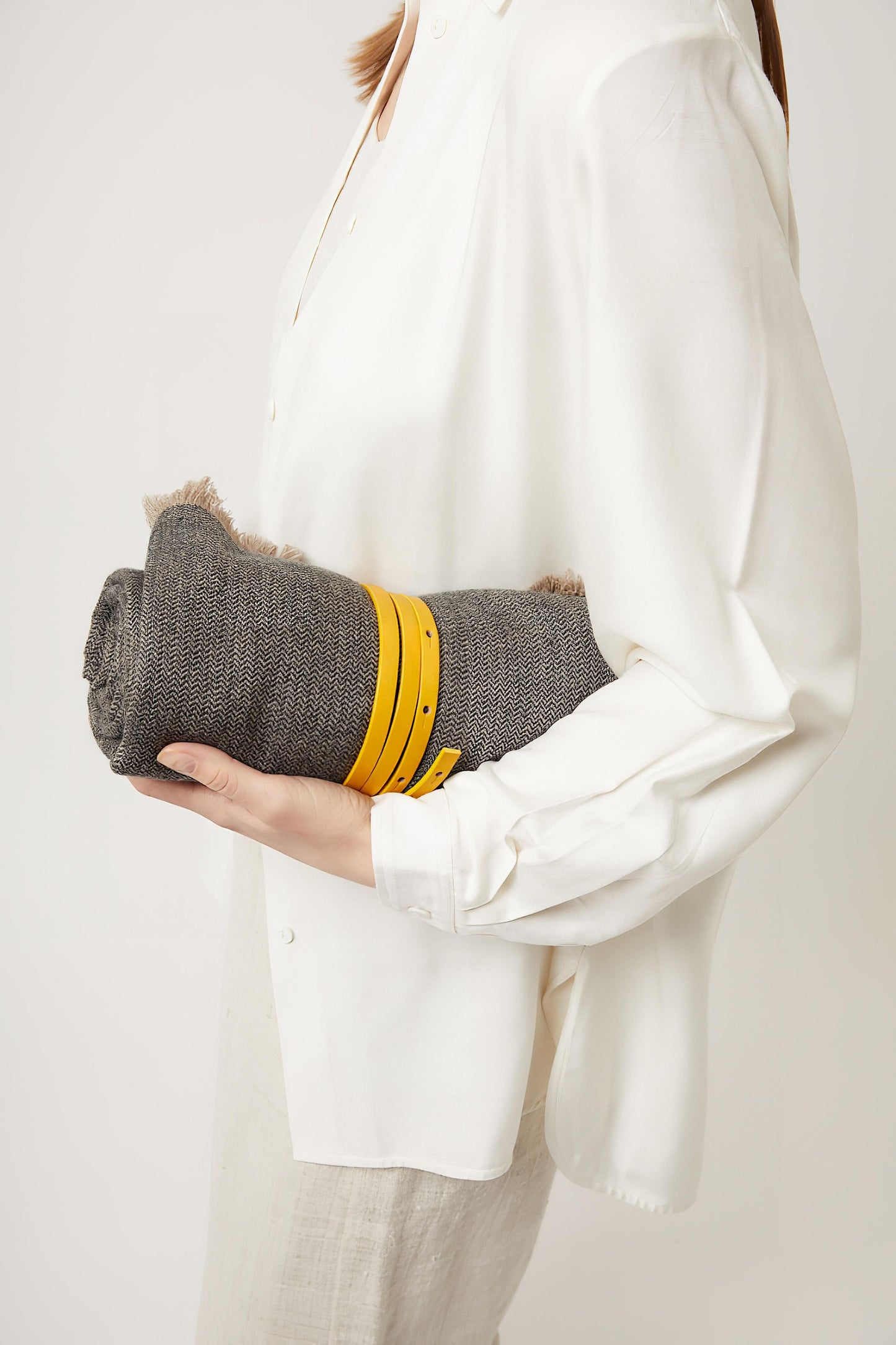 A woman holding a saan charcoal and taupe throw, tied with a gold leather belt