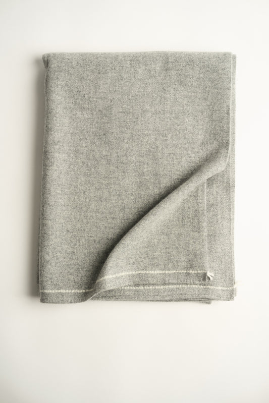 A folded soft grey throw with hand-rolled edges and a contrast color stitch line.